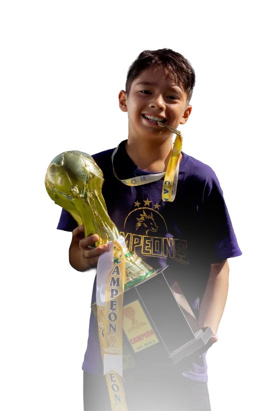 Niño sonriente sosteniendo un trofeo dorado de fútbol en un campo de juego durante el curso de verano de Carax